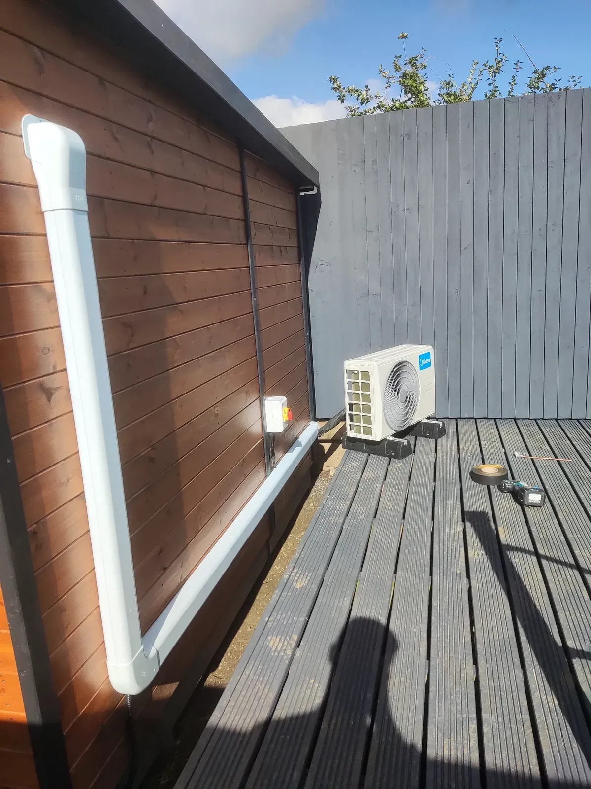 Outdoor air conditioning condenser installed beside a garden room with trunking and isolator
