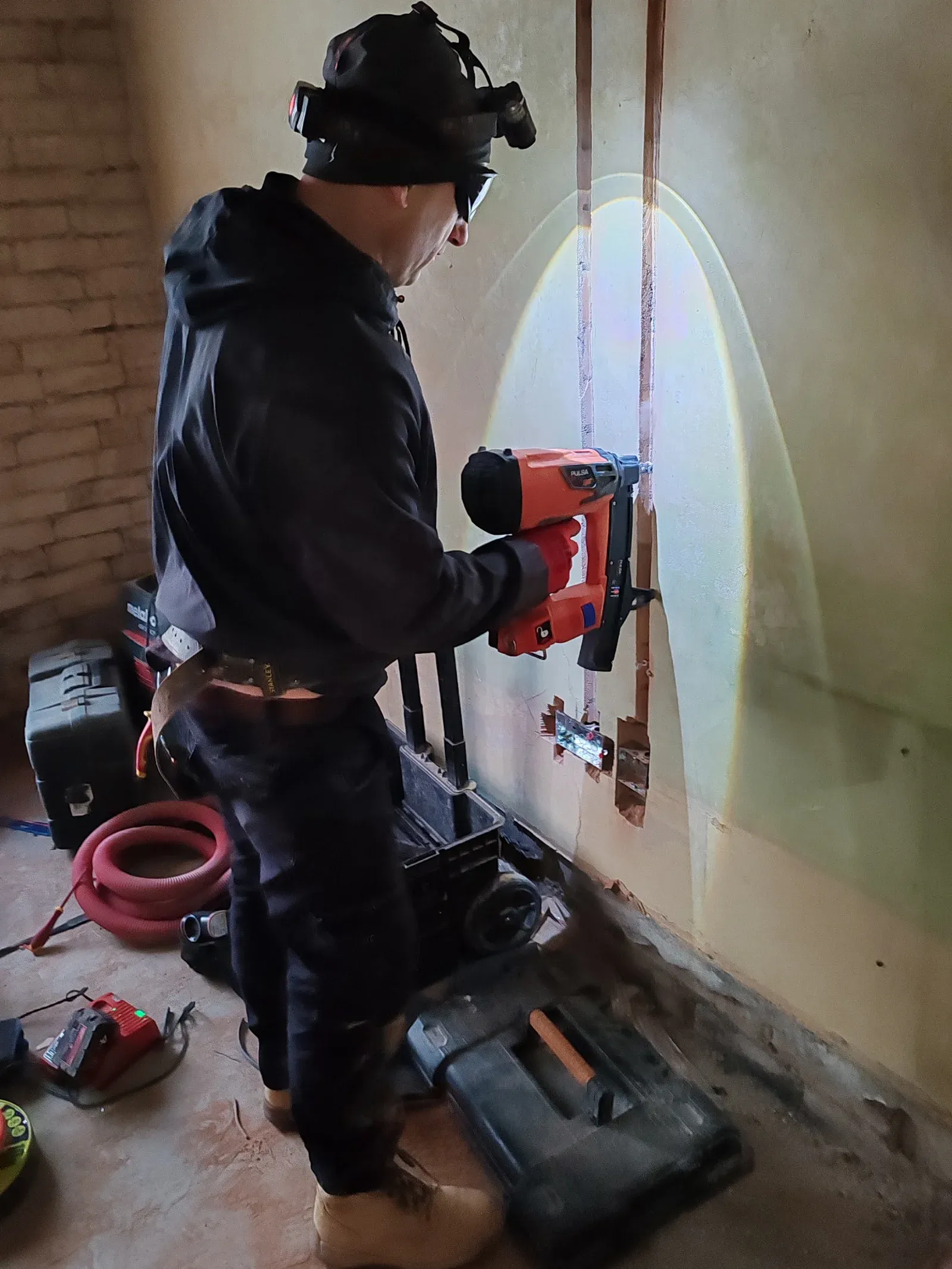 Electrician using a Pulsa pin gun to clip new cables during first-fix rewire on a 3-bedroom house in Leicester