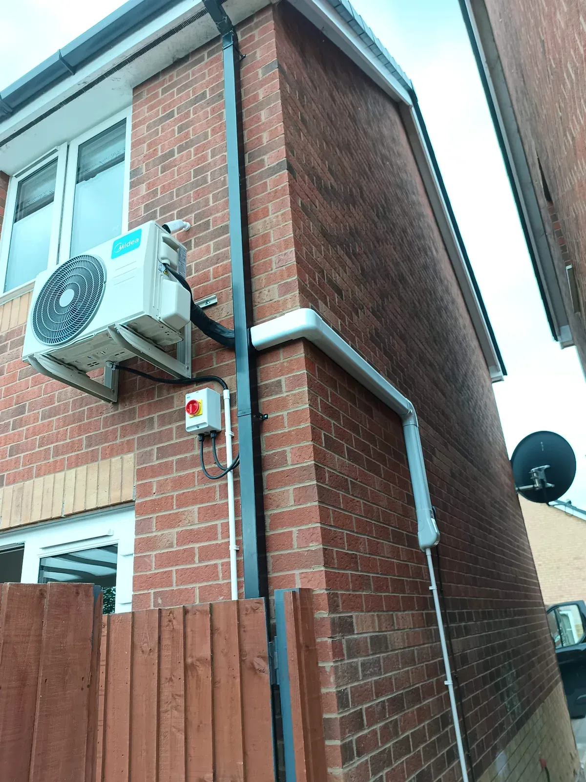Midea outdoor air conditioning unit on wall brackets with external pipework and isolator