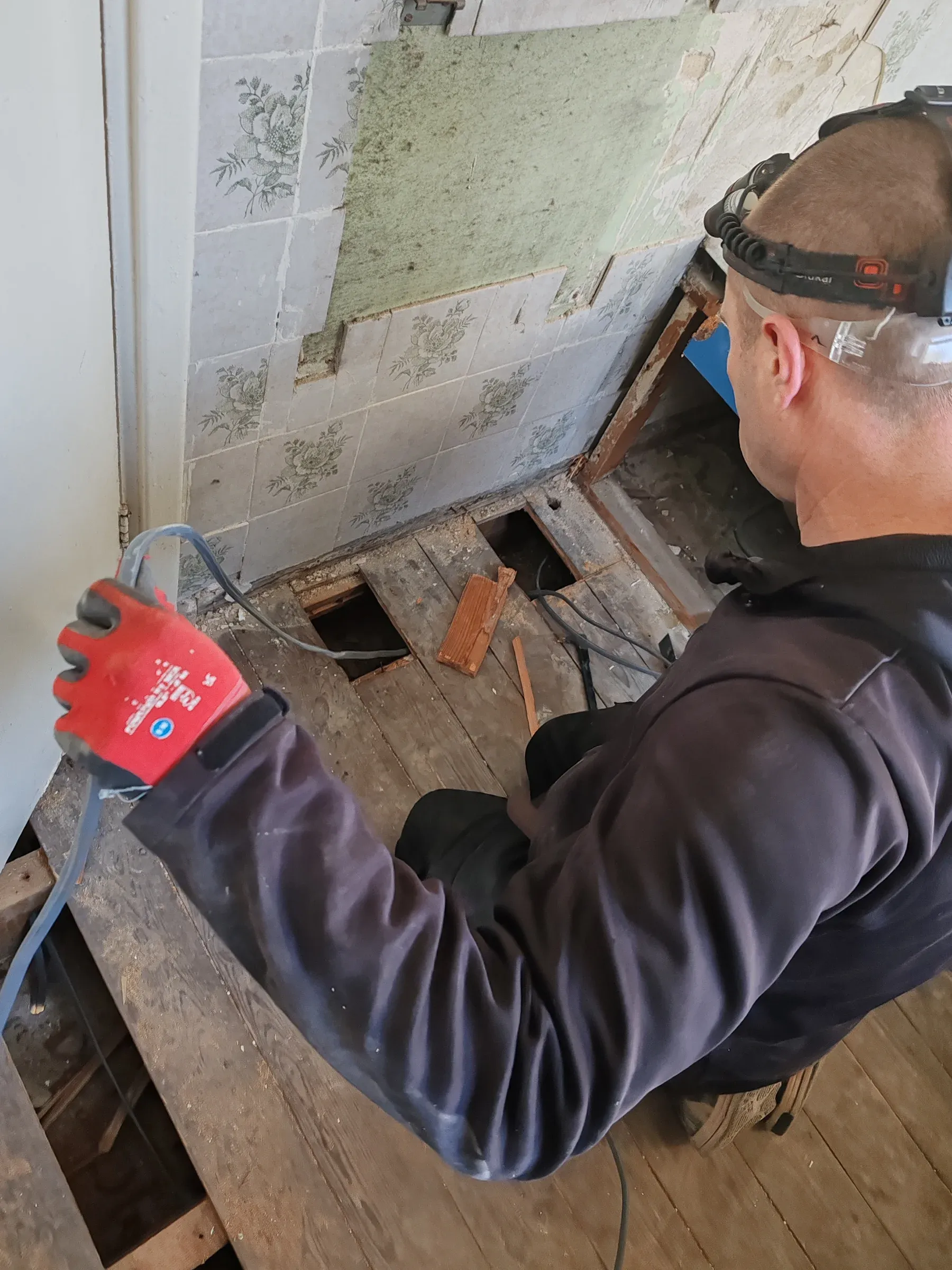 Electrician pulling new cables under lifted floorboards during a full house rewire
